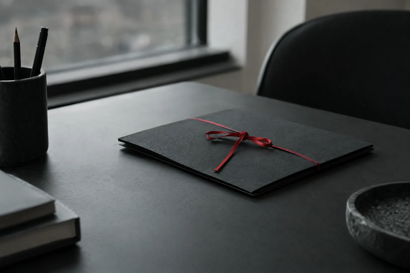 A closed black folder with a red ribbon on a desk