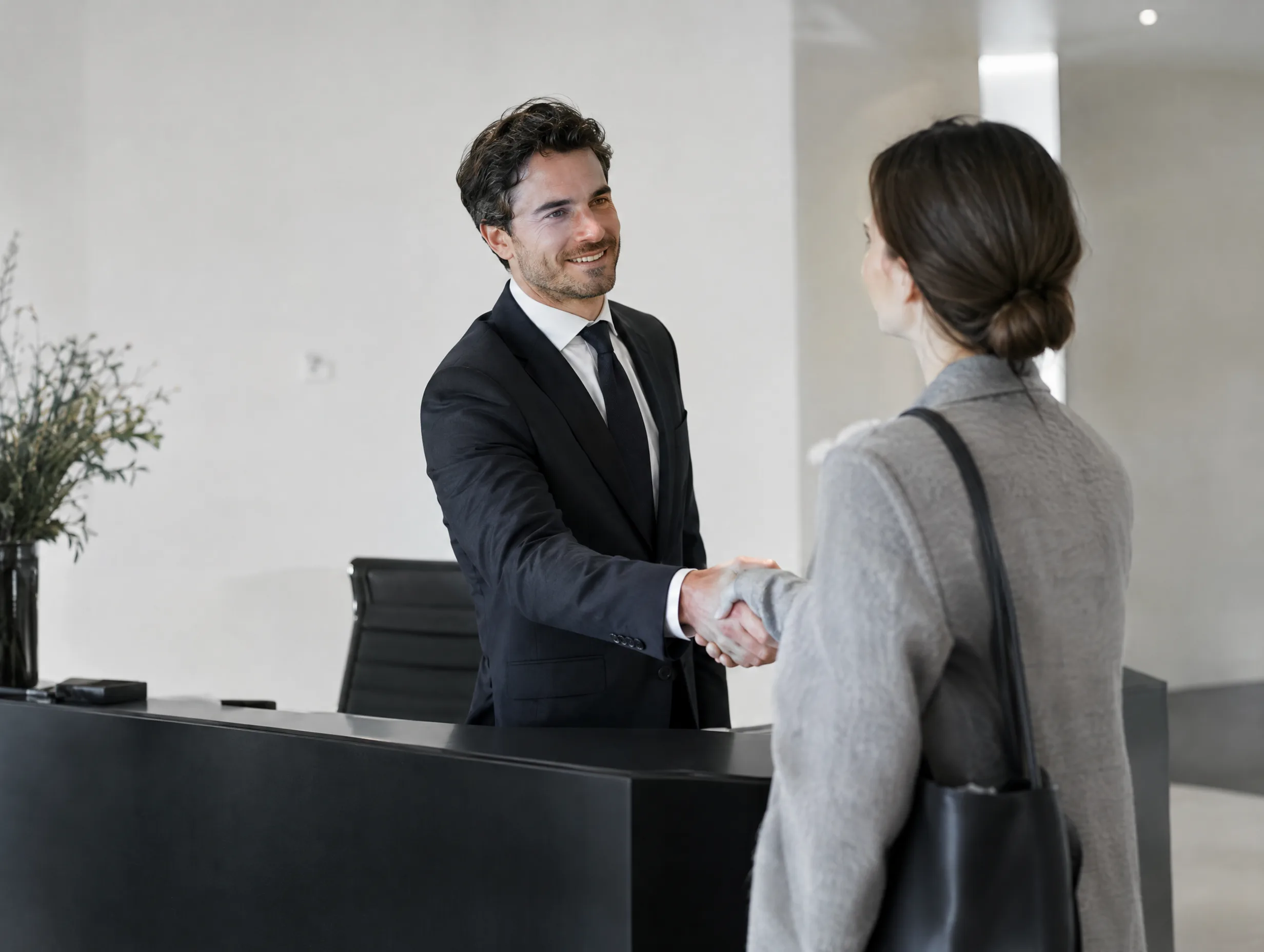 A partner welcoming a client at a minimal black reception desk